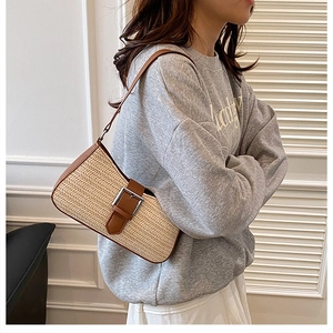 Detail view of woven straw baguette bag with brown faux leather trim and silver buckle