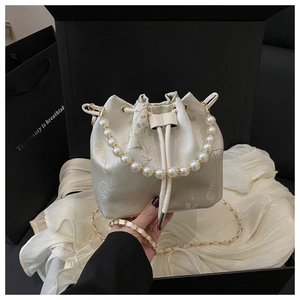 Detail of cream bucket bag with floral embroidery, pearl handle and chain strap