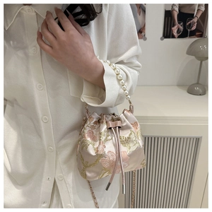 Close-up of floral embroidery detail and pearl handle on a satin bucket bag