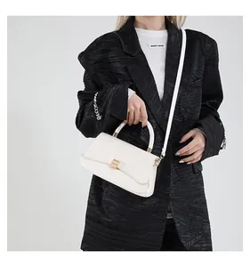 Detailed view of white leather baguette bag with gold buckle on black blazer