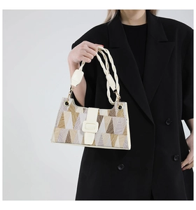 Detail of geometric patchwork underarm bag with woven leather handle and metal hardware