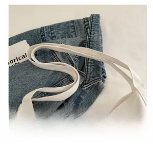 Macro detail of reinforced canvas handle stitching on a white tote bag against denim