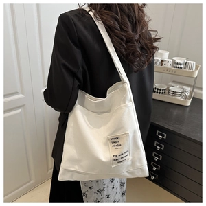 Detail of white canvas tote bag featuring creative text patch and thick texture