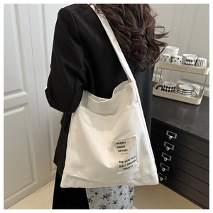 Detail view of white canvas tote bag with side patch and wide shoulder strap