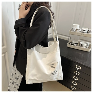 Detail of white canvas tote bag featuring external pocket and decorative text patch