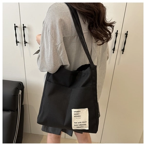 Detail of black canvas tote bag with white text patch shown on model in home setting