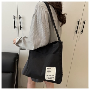 Detail view of black canvas tote bag showing side pocket and white graphic text patch