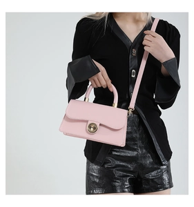 Pink leather handbag with gold twist lock shown styled on a model with black outfit