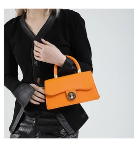 Detail of the bright orange leather handbag featuring a large round gold metal lock