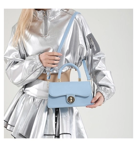 Detail of light blue crossbody bag with gold round lock worn by model in silver outfit