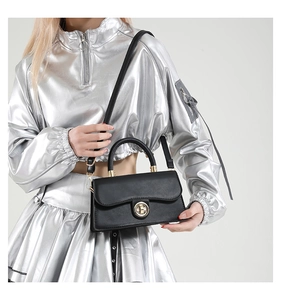 Detail of a chic black crossbody bag with a gold metal lock styled on a silver metallic outfit