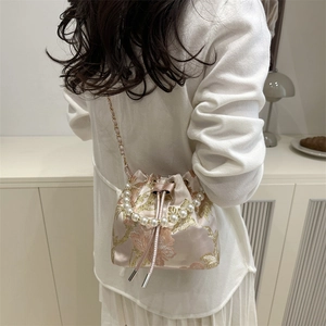 Elegant bucket bag with pearl handle and golden floral embroidery on woven fabric