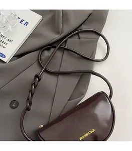 Detail of dark brown leather crescent bag featuring a unique braided shoulder strap