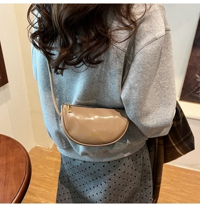 Close-up of nude half-moon crossbody bag with glossy patent leather and gold zipper
