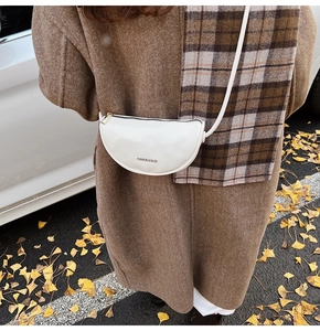Detail of white PU leather crescent moon bag with golden zipper in autumn street setting