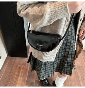 Close-up of black leather crescent shoulder bag styled with beige knit sweater