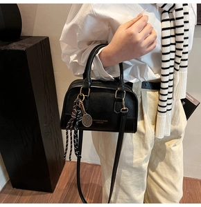Detail of black leather handbag with golden hardware and stylish tennis racket charm strap