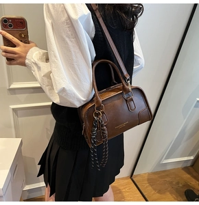 Detail of dark brown leather Boston bag with gold logo and woven tassel accessory