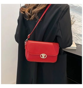 Détail d'un sac à bandoulière en cuir rouge avec fermoir doré sur un manteau noir