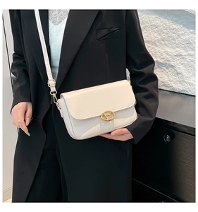 Détail du sac à bandoulière blanc crème avec fermoir doré sur un blazer noir