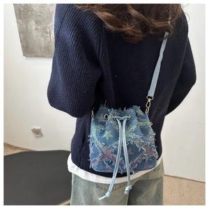 Detail of blue denim bucket bag featuring colorful star prints and fringe tassel edges