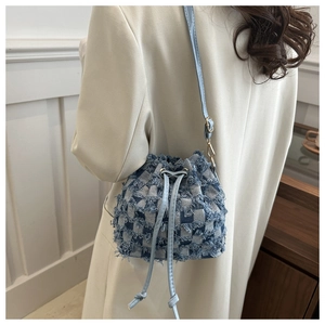 Détail du sac seau en denim à carreaux bleu clair avec franges et bandoulière en cuir
