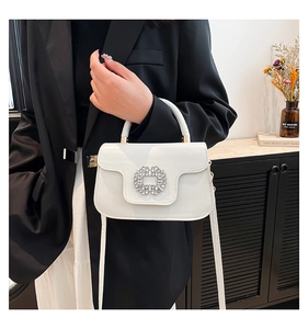 Detail of cream-white handbag featuring a sparkling crystal-encrusted round buckle closure