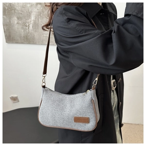 Détail du sac bandoulière gris texturé avec bordure en cuir brun et boucles dorées