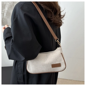 Détail du sac à bandoulière tissé crème avec bordure en cuir marron sur un manteau noir