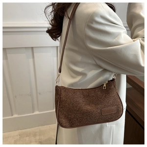 Detail of brown woven baguette bag showing the leather logo tag and gold-tone metal hardware