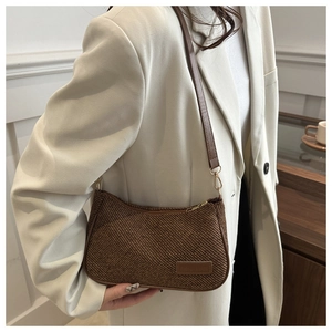 Détail du sac sous le bras en texture tressée marron avec logo en cuir et zip doré