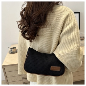 Detail of black woven shoulder bag with brown leather trim and metal hardware hooks