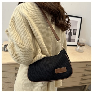 Detail of black corduroy shoulder bag with brown leather label and stylish strap