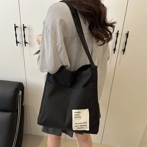 Black high-capacity canvas tote bag for women featuring a minimalist white woven patch label
