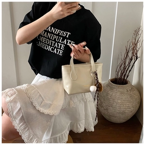 Close-up of cream faux leather handbag with trendy baseball pendant and woven rope detail