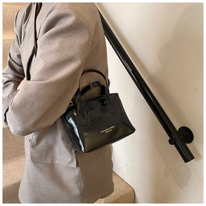 Close-up of a glossy black patent leather mini tote bag with stylish white typography