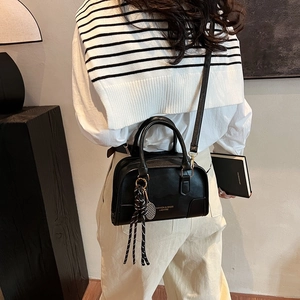 Minimalist black leather handbag with tennis racket charm and adjustable strap shown on model