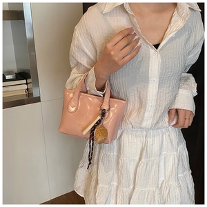 Detail of light pink glossy handbag with decorative charms held by a model in a white outfit