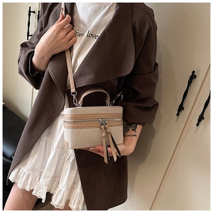 Detail van een beige canvas boxtas met lange kwastjes, lederen bekleding en handvat