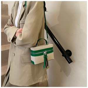 Detail of canvas and green leather crossbody bag worn with a beige blazer suit
