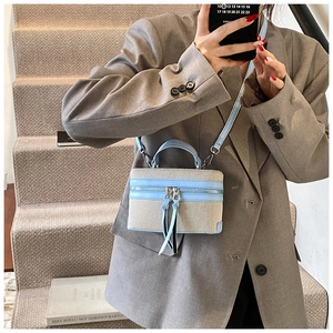 Detail van tweekleurige box-tas van beige canvas met blauw leer en lange kwastjes aan rits