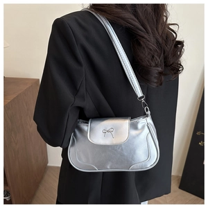 Detail of silver shoulder bag with metallic bow buckle shown on black blazer suit