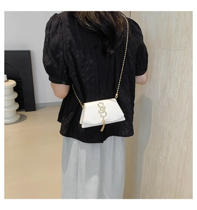 Detail of white leather mini flap bag with gold S-logo, tassel, and chain strap on model