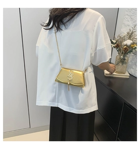 Detail shot of golden metallic crossbody bag with SS logo and tassel on a model