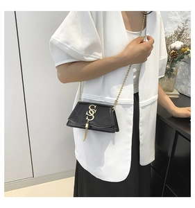 Detail view of black leather crossbody bag featuring gold S logo and chain strap