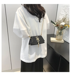 Detail of a black patent leather shoulder bag with gold hardware and tassel detail