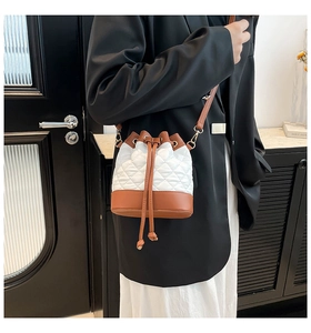 Close-up of quilted drawstring bucket bag featuring white embroidery and brown leather trim