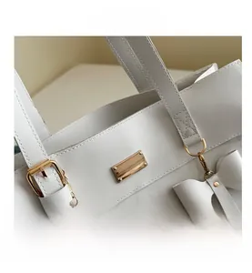 Detail of white leather tote bag with gold buckle, bow charm and reinforced stitching