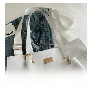 Detail view of white leather tote with golden plaque, bow charm, and wide textile strap