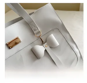 Detailed view of leather tote bag with golden logo plate and matching bow charm accessory